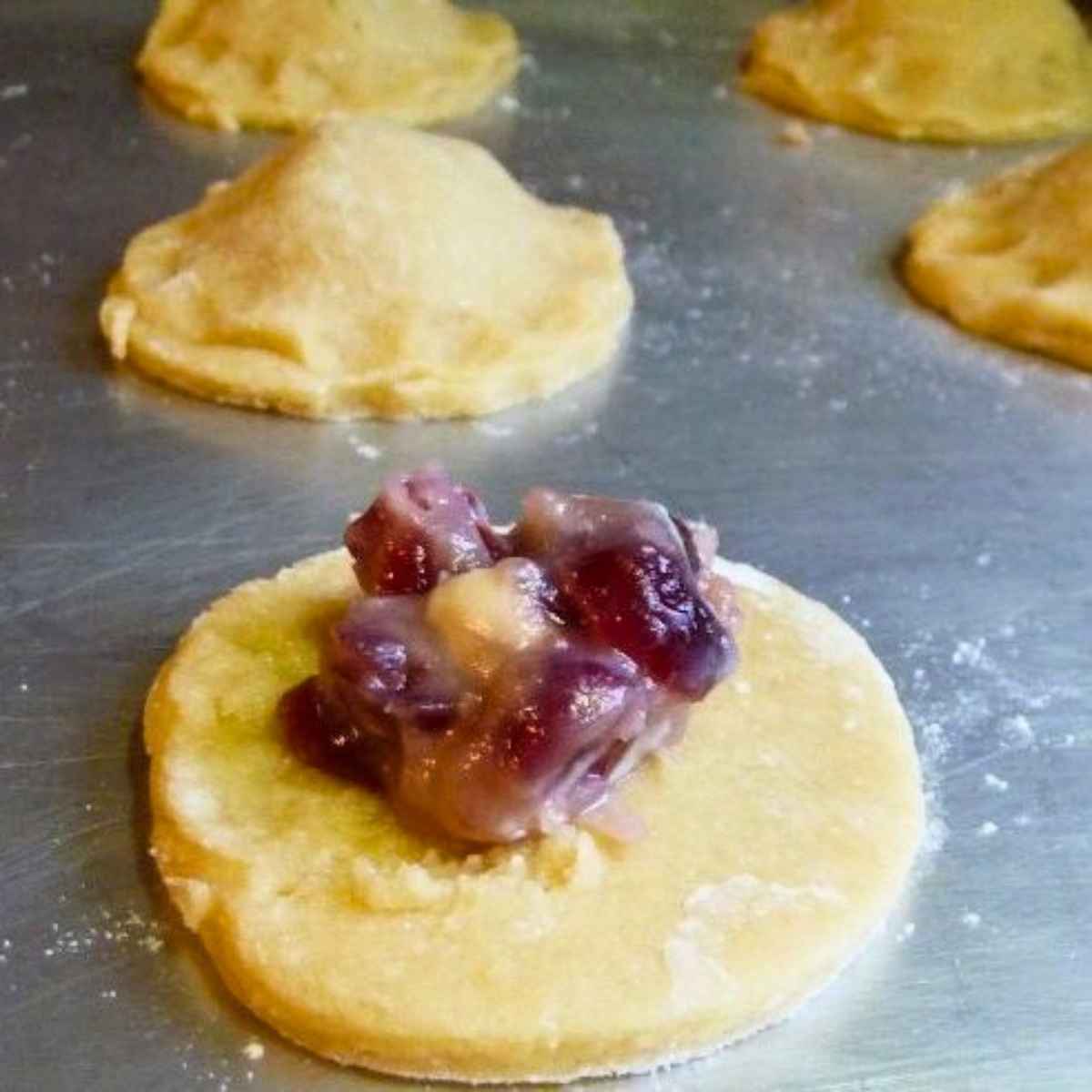 Cookie dough circles with craisin filling in the center on a baking sheet.