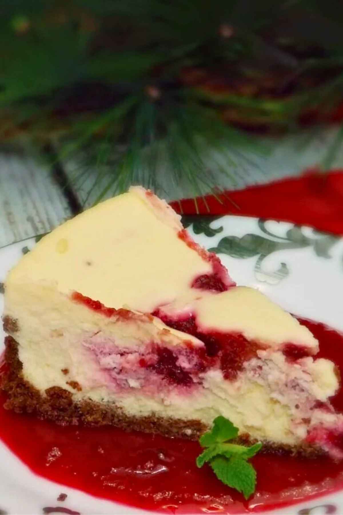 One slice of Cranberry Swirl Cheesecake sitting on a pool of blended amaretto cranberry sauce garnished with fresh mint on a silver trimmed dessert plate