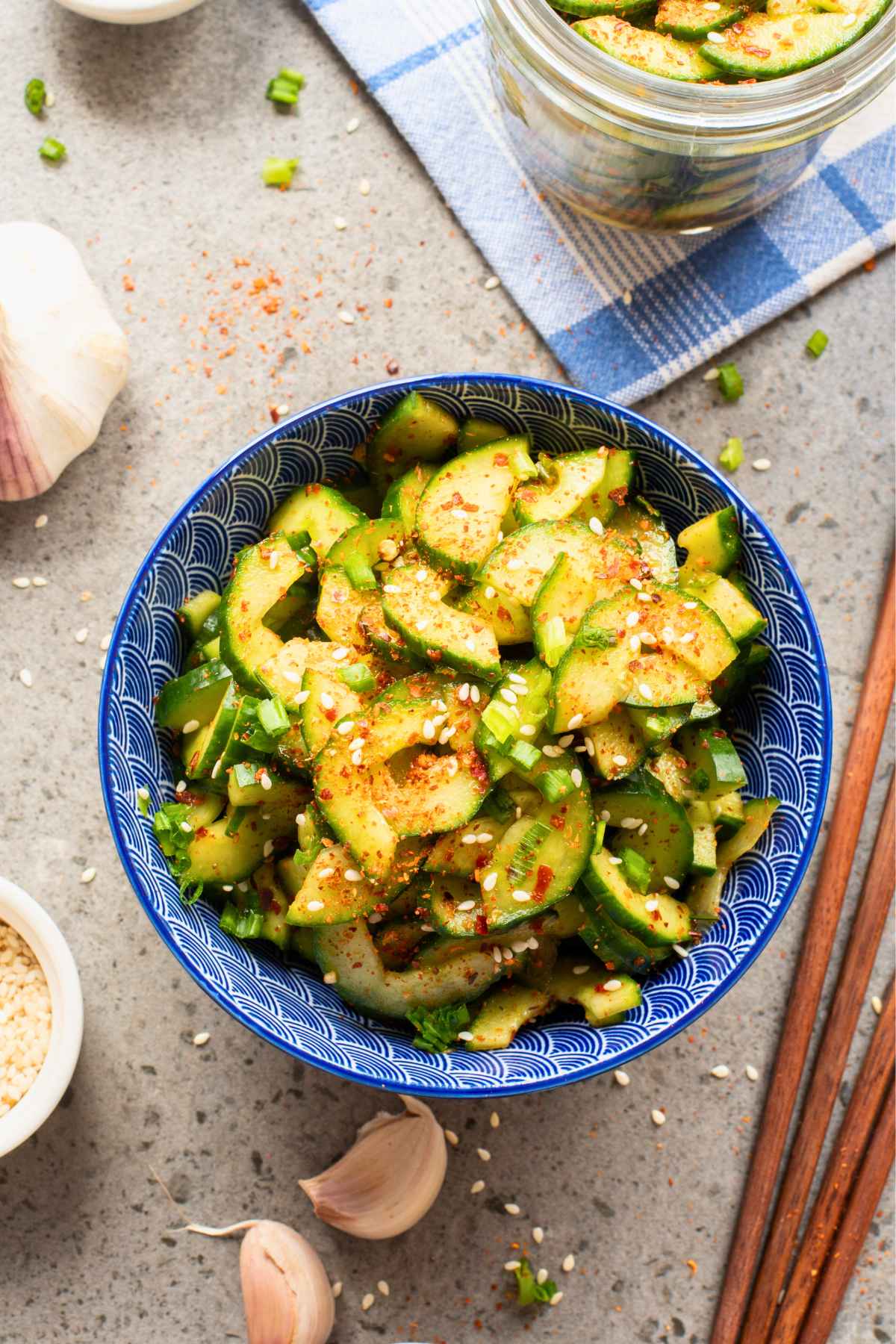 Overhead image of a blue serving bowl filled with cucumber kimchi sprinkled with sesame seeds.
