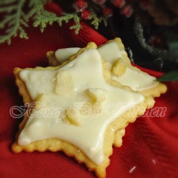 Two star shaped eggnog cookies with rum glaze sprinkled with macadamia nuts on a red cloth.