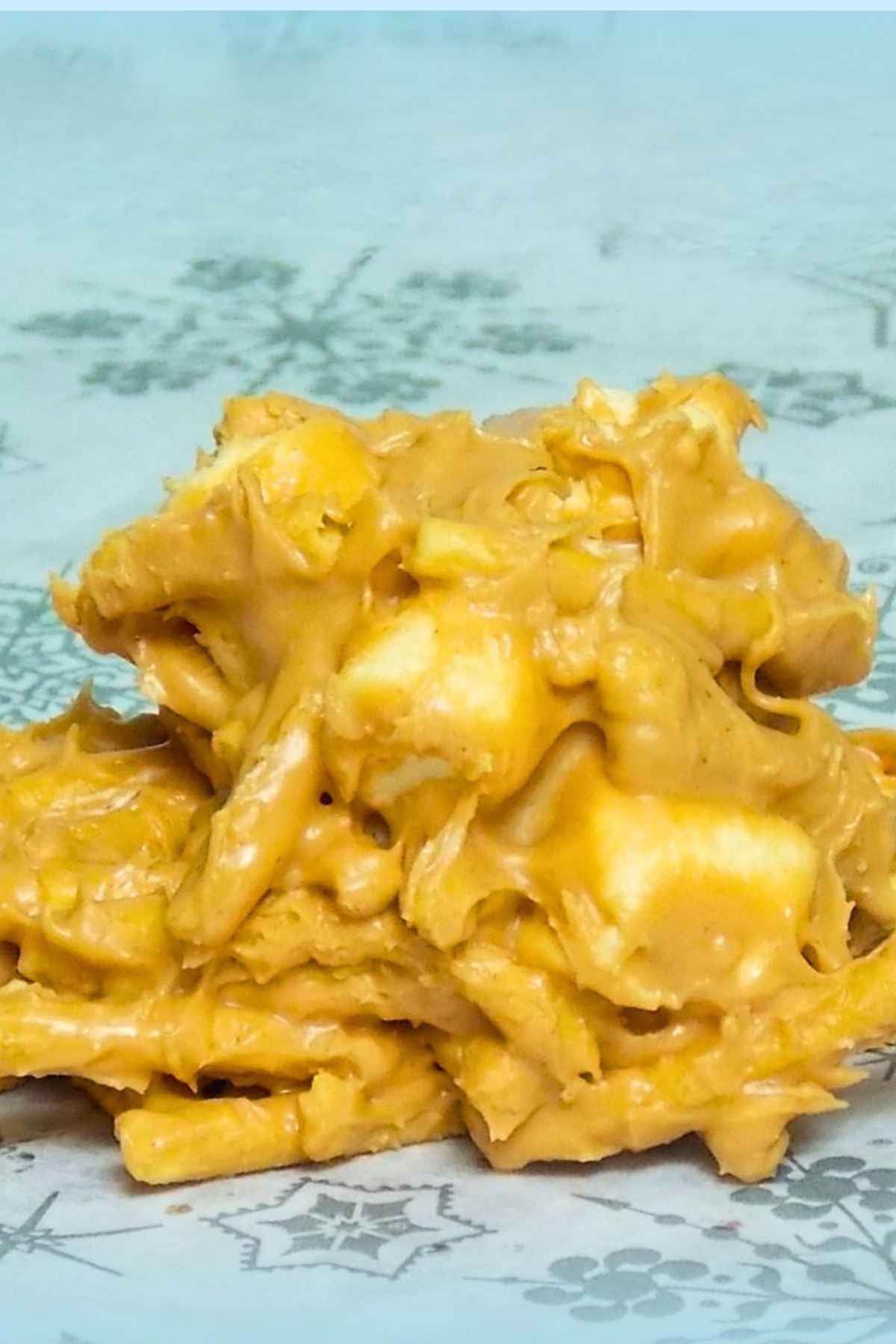A closeup of a butterscotch haystack cookie made with melted butterscotch chips, chow mein noodles, and mini marshmallows, piled into an irregular mound on a snowflake patterned plate.