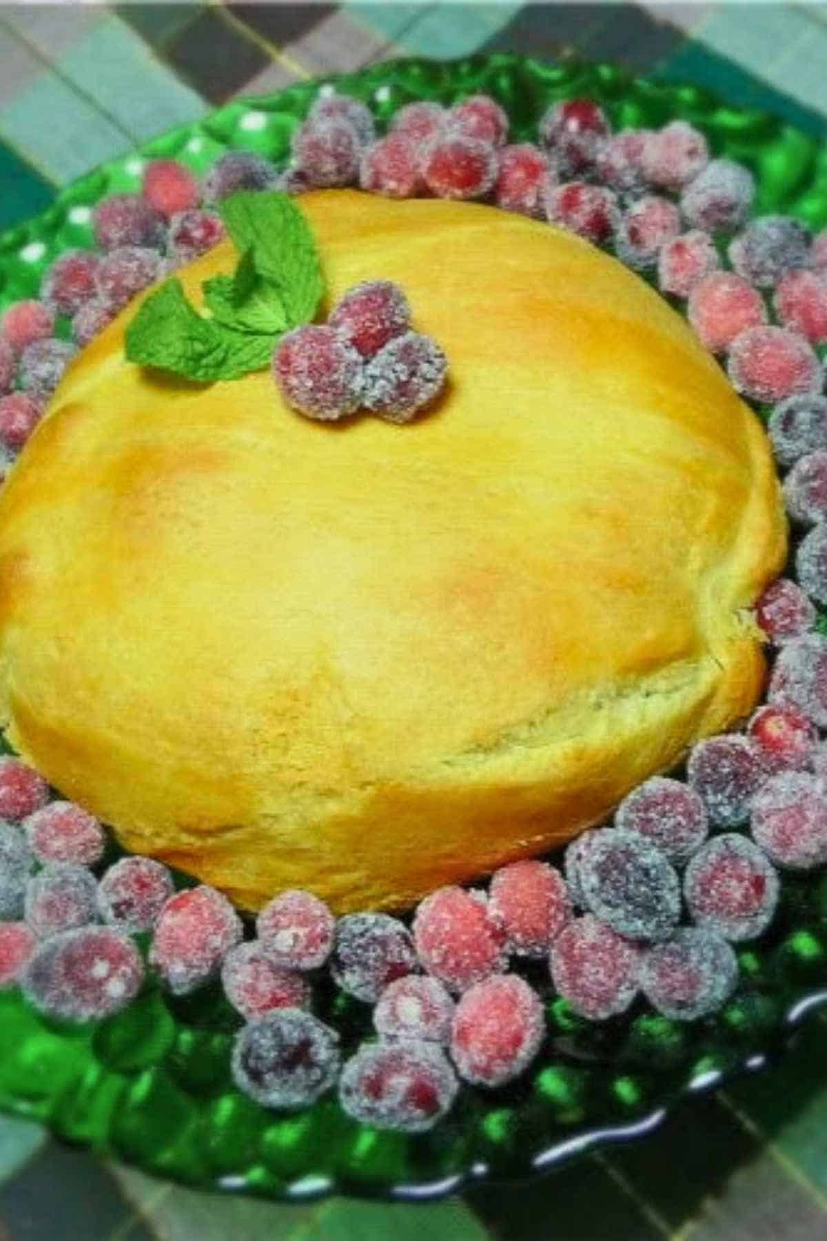 Golden brown Maple Pecan Baked Brie on a green serving platter surrounded by sugared cranberries and garnished with mint.