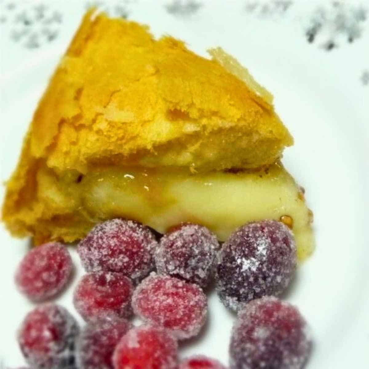 A serving plate with a wedge of crescent wrapped cheese and a side of sugared cranberries.