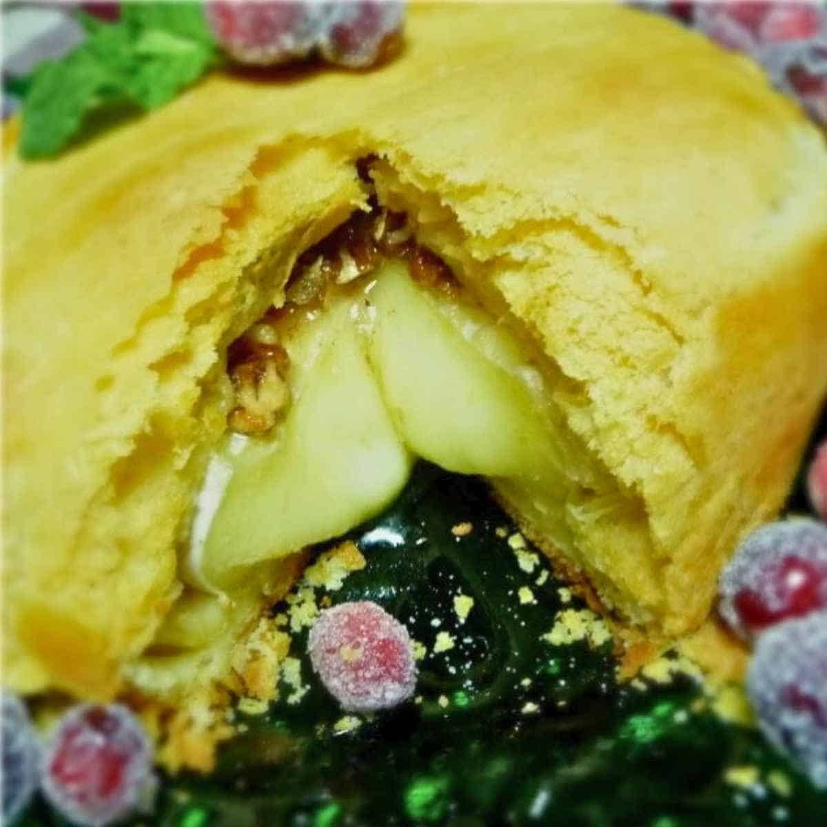 Crescent wrapped brie cheese topped with pecans with a wedge cut out showing melty cheese flowing from the dough.