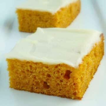 Two pieces of pumpkin sheet cake topped with cream. cheese icing on a white plate.