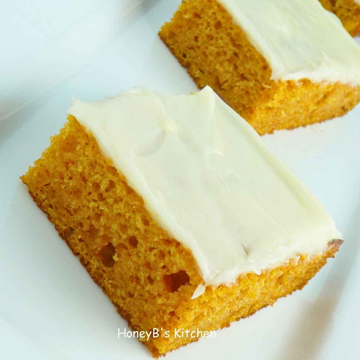Two pieces of pumpkin sheet cake topped with cream. cheese icing on a white plate.
