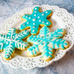 Three decorated snowflake cut out sugar cookies on a white plate.