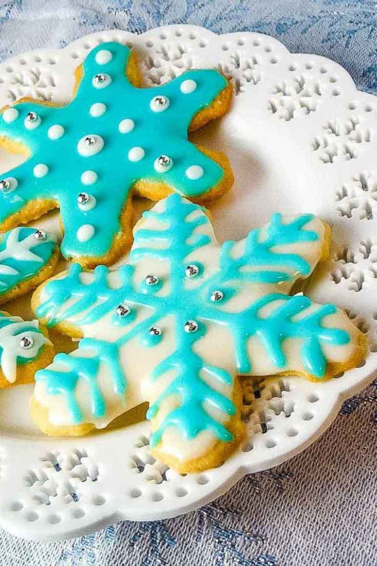 Upclose snowflake cut out sugar cookies on a white snowflake plate.