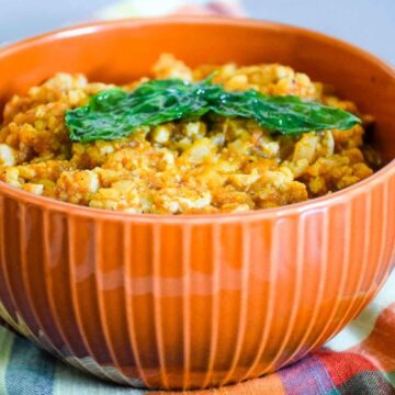 An orange bowl filled with Spanish Cauliflower Rice topped with fried basil leaf.