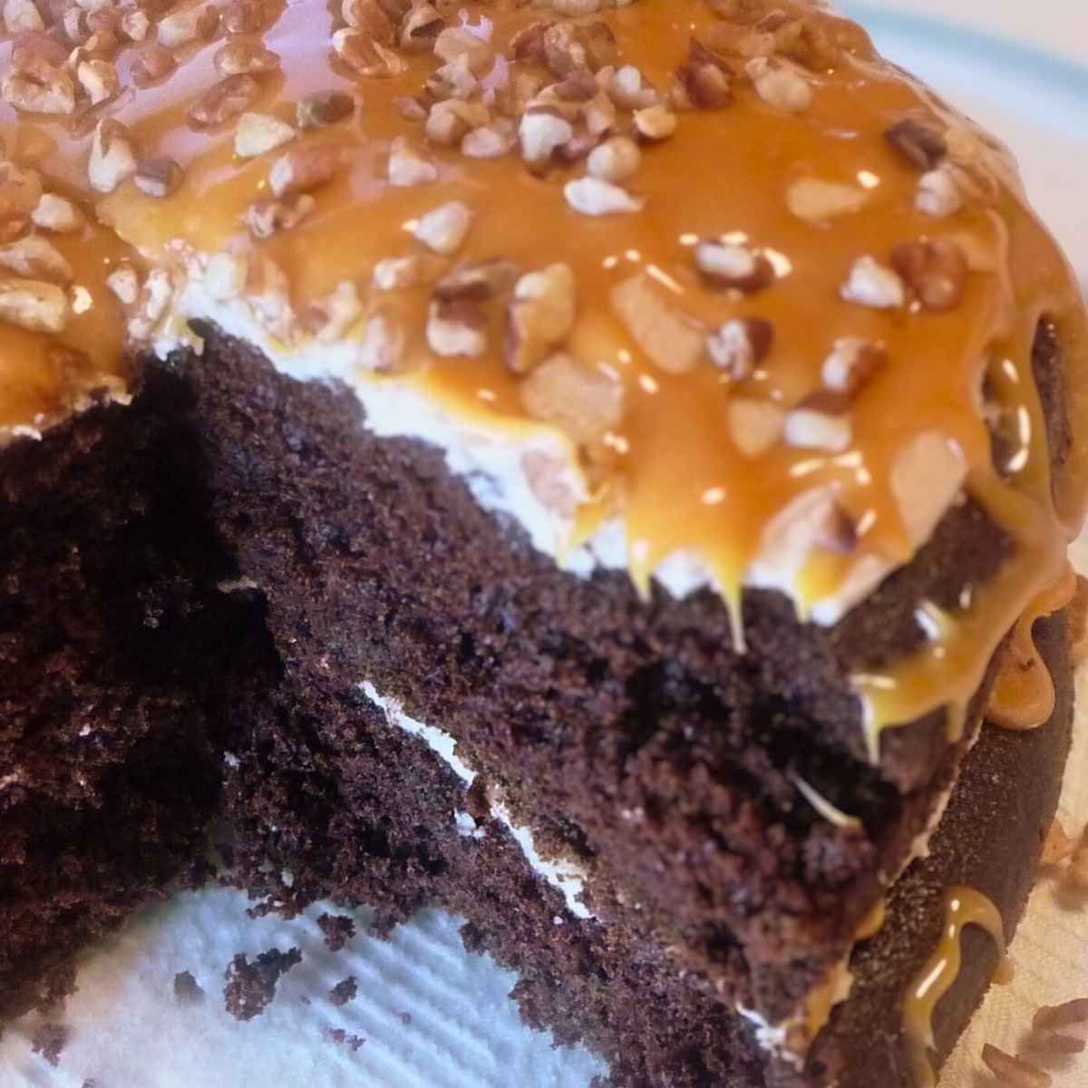 A chocolate layer cake with caramel frosting and caramel drizzle topped with chopped pecans.