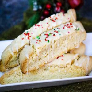 A white plate stacked with eggnog biscotti drizzled with a white glaze and red, green, and white sprinkles.