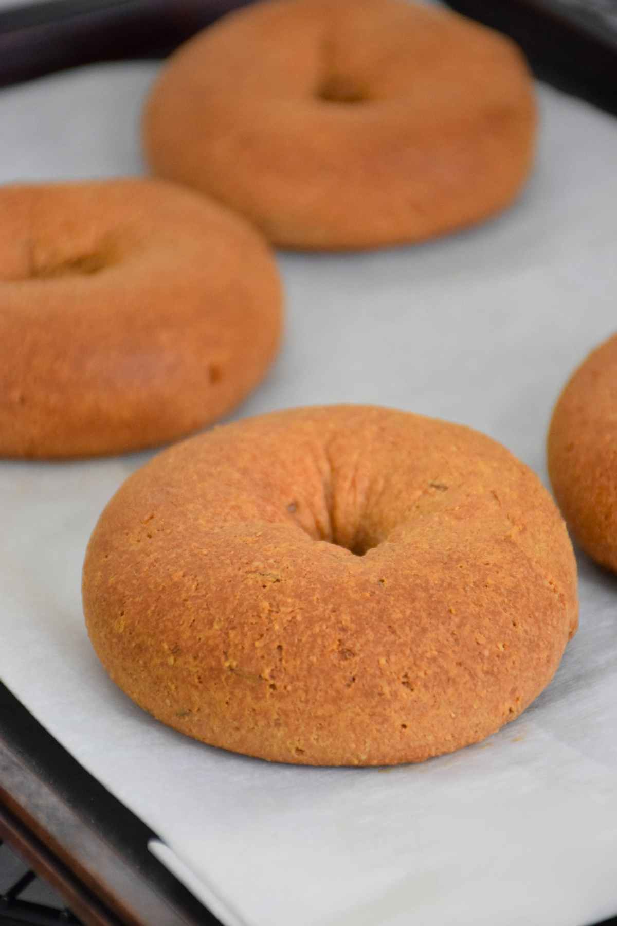 Freshly baked keto bagels with a golden crust and visible flecks of seasoning on a parchment paper lined baking sheet.