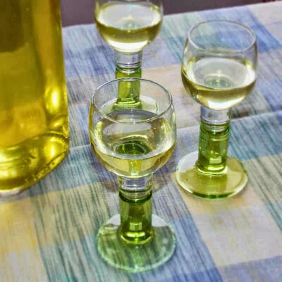 Limoncello glasses filled with homemade limoncello recipe on a blue and yellow checkered napkin.