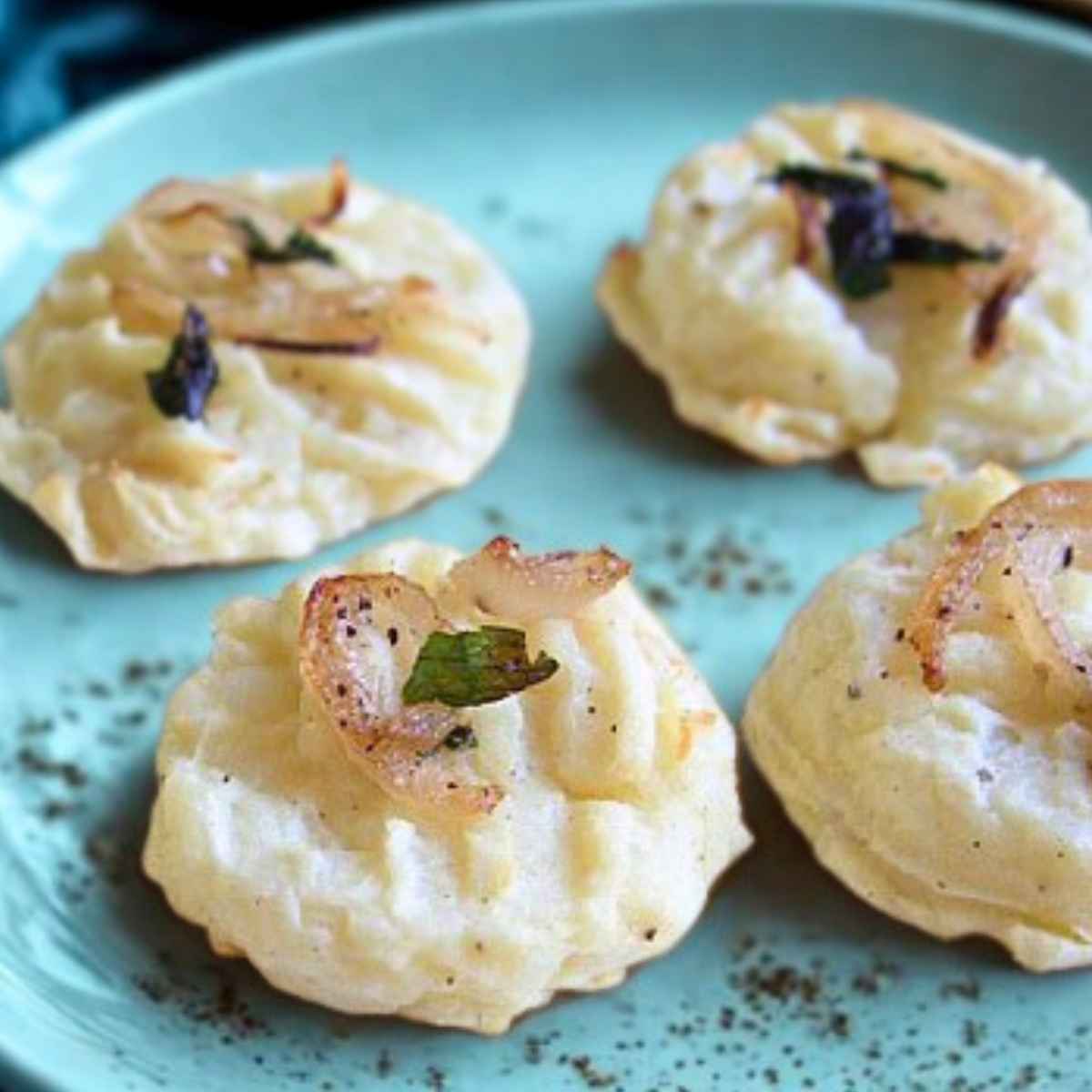 Upclose image of four mashed potato patties garnished with onion slices on a pale blue plate.