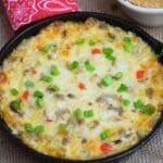 A cheesy Philly cheesesteak dip in a cast-iron skillet topped with melted provolone, browned beef, and fresh sliced green onions.