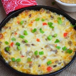 A cheesy Philly cheesesteak dip in a cast-iron skillet topped with melted provolone, browned beef, and fresh sliced green onions.