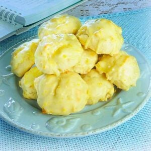 A blue plate wit stacked pineapple orange cookies with an orange glaze flecked with ornage zest.