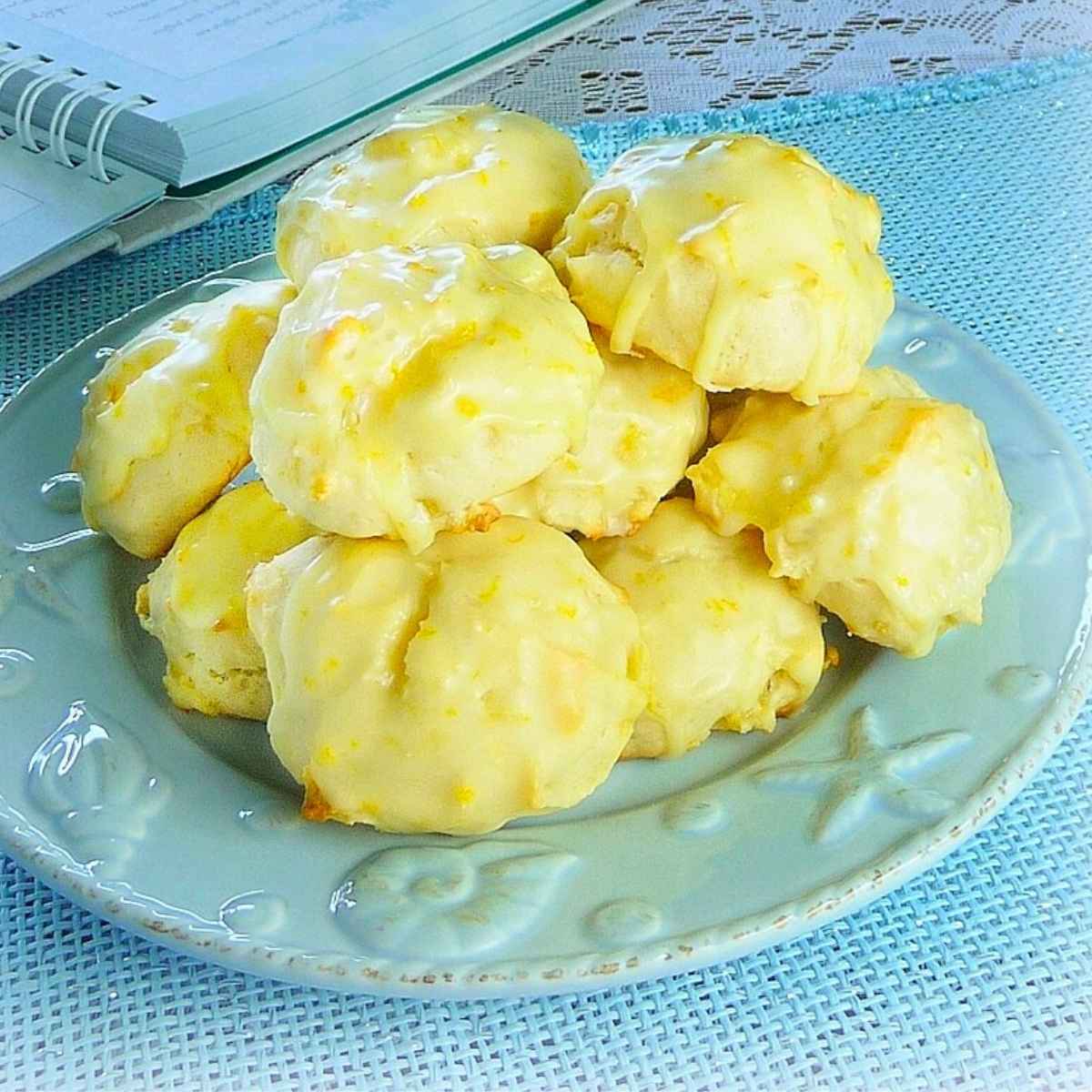 A blue plate wit stacked pineapple orange cookies with an orange glaze flecked with ornage zest.