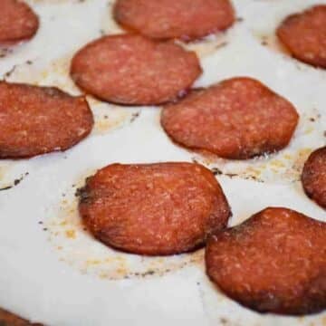 Crispy, golden brown baked salami cips arranged on a parchment-lined baking sheet.