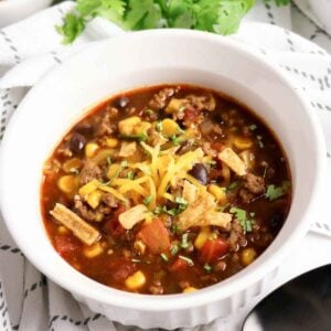 A bowl of hearty beef enchilada soup with corn, black beans, and melted cheese garnish.