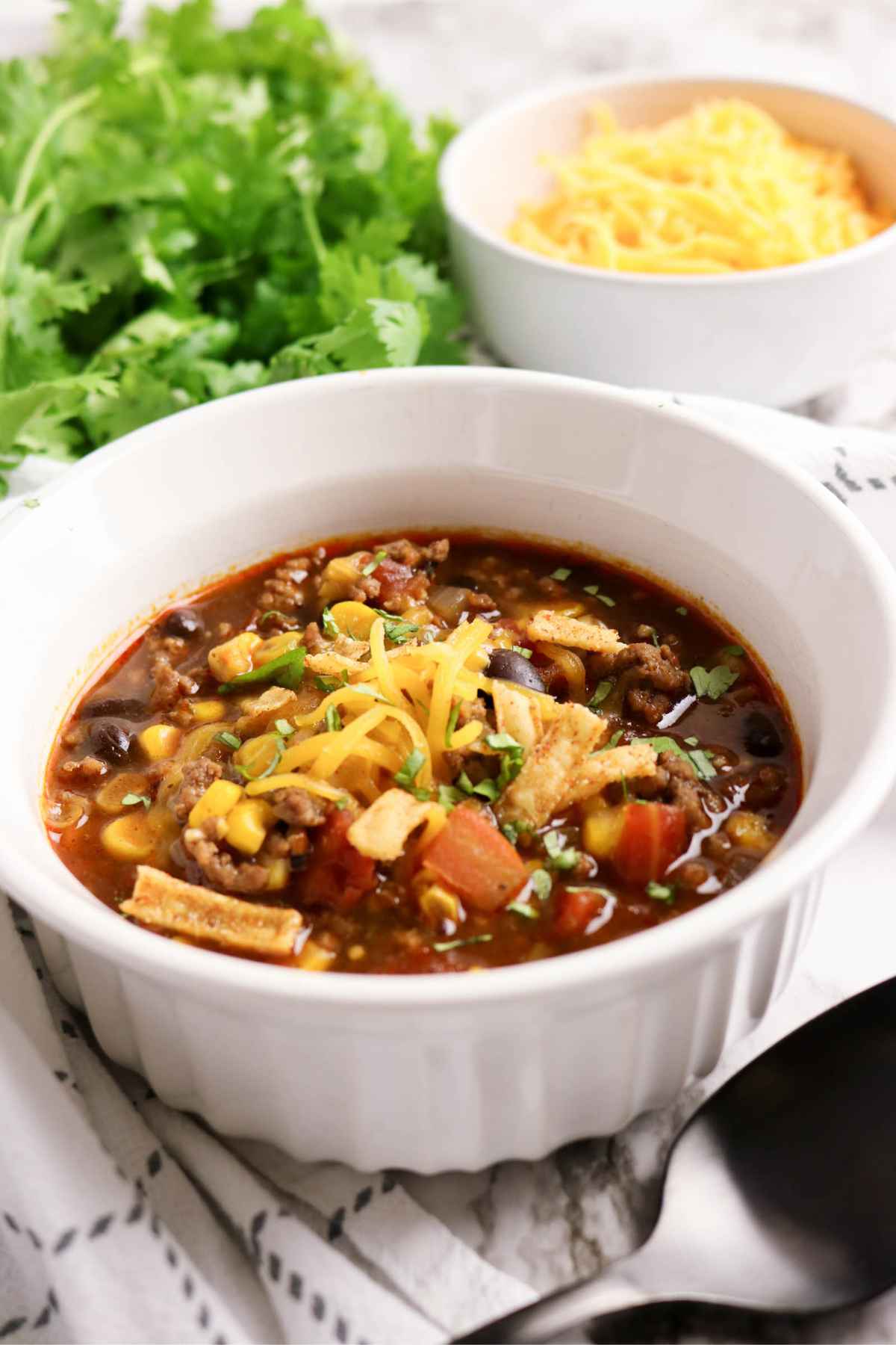 A bowl of hearty beef enchilada soup with corn, black beans, and melted cheese garnish.