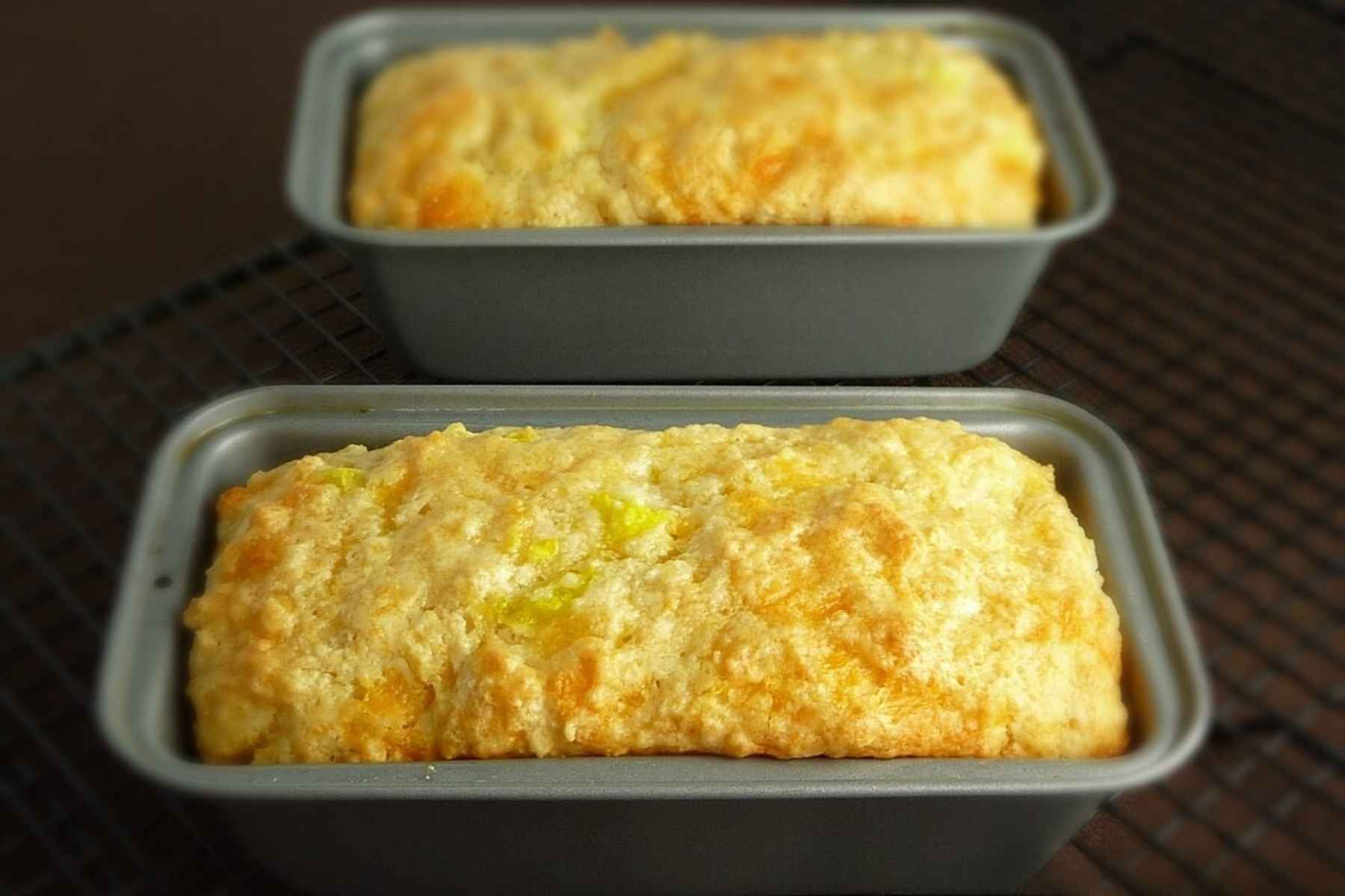 Two loaves of golden brown quick bread in baking dishes on a cooling rack.