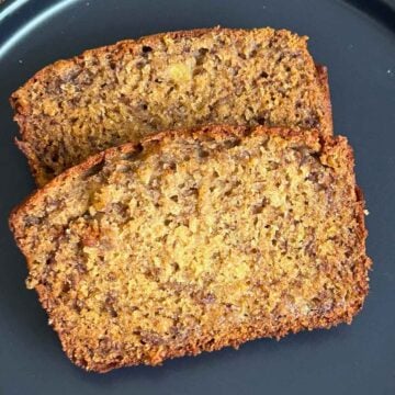 Two thick, moist slices of Banana Bread with Browned Butter stacked on a dark plate, showing a soft crumb and golden brown crust.