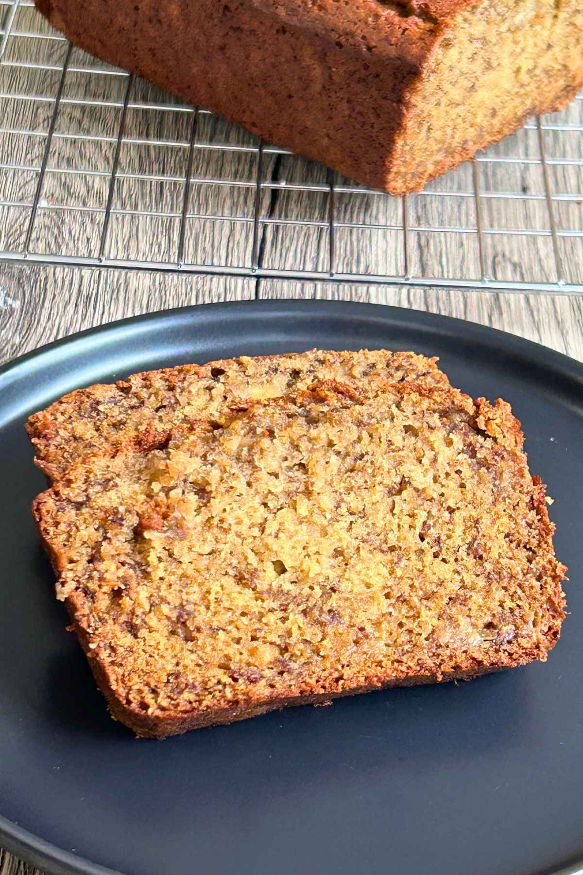 Thick slices of browned butter banana bread on a dark plate, showing a tender crumb and golden crust, with the rest of the loaf on a wire cooling rack in the background.
