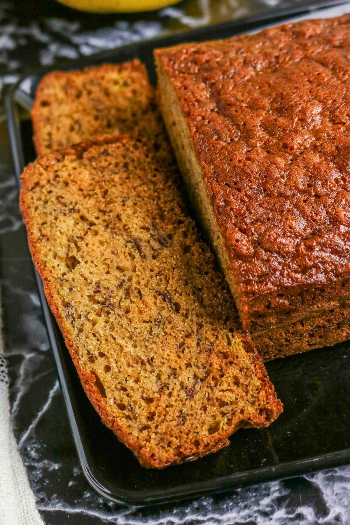 Two slices of Browned Butter Banana Bread layered on a black serving dish against a neutral background.