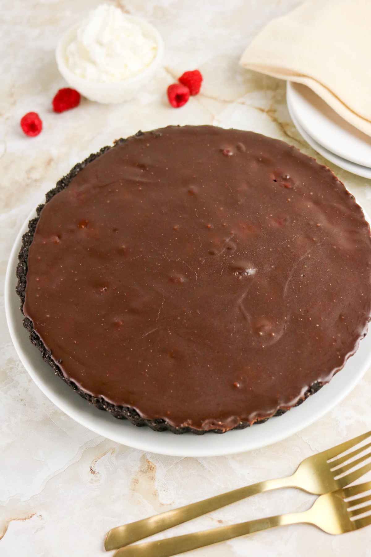 A whole chilled chocolate tart with a dark cookie crust on a white plate.