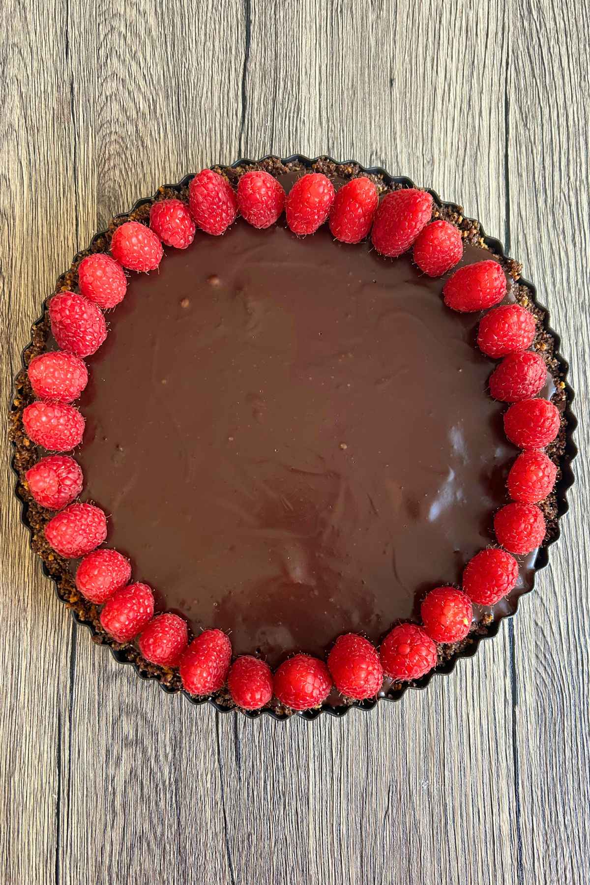 An overhead view of a whole chocolate ganache tart ringed with fresh raspberries.