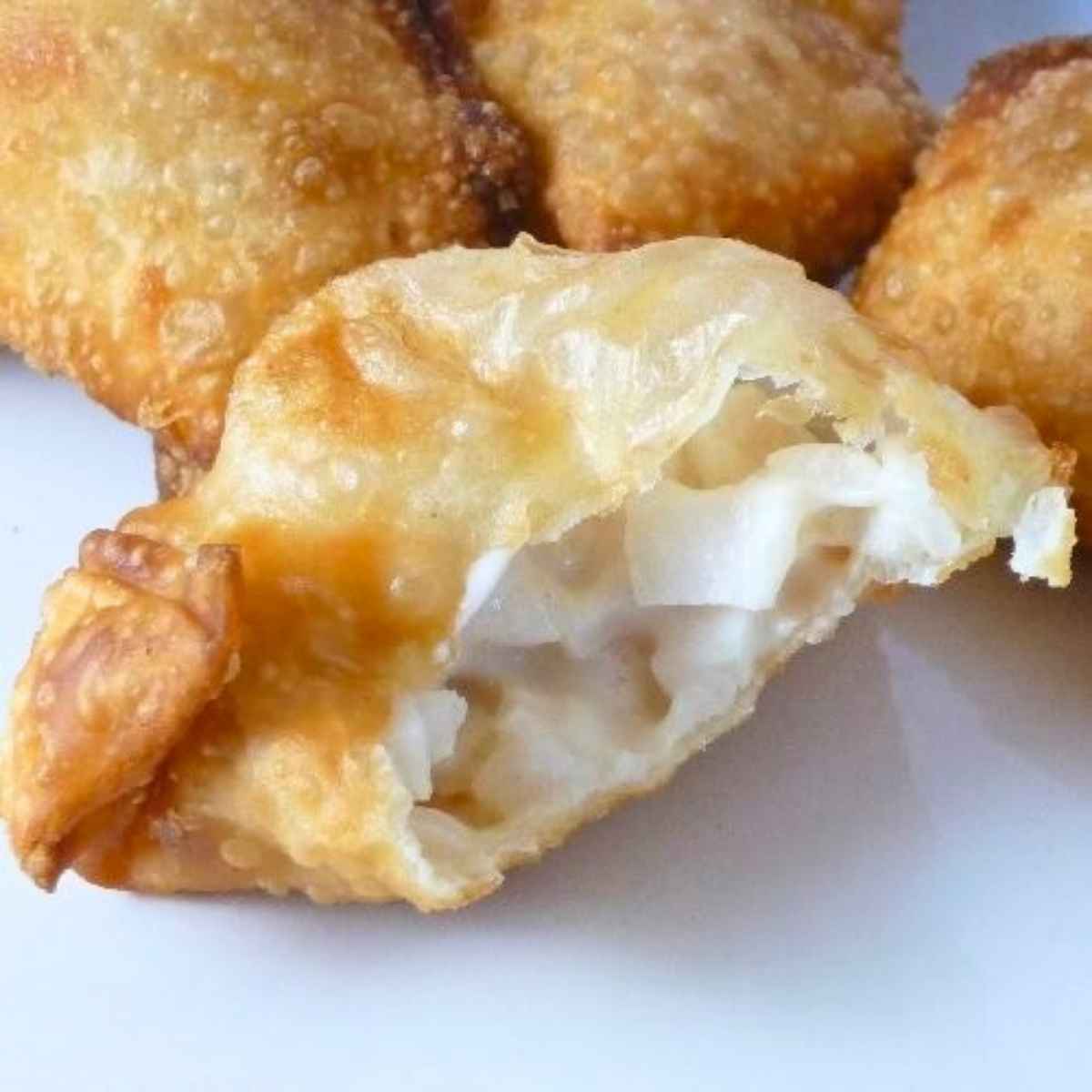 Golden brown, crispy fried wonton and cream cheese appetizer with a bite taken from it.