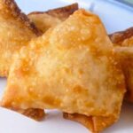Golden brown, crispy fried crab rangoons stacked closely together.