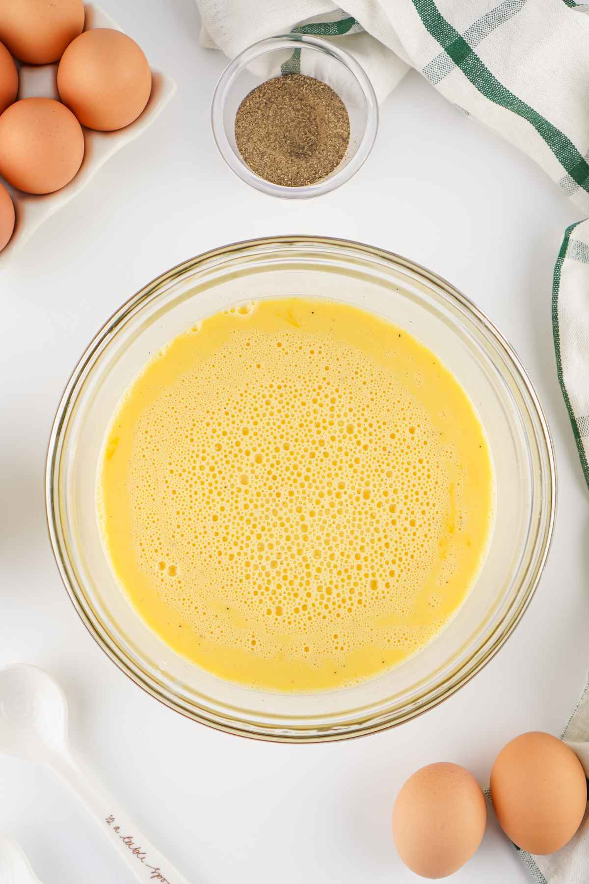 A glass bowl filled with whisked, frothy yellow liquid on a white counter.