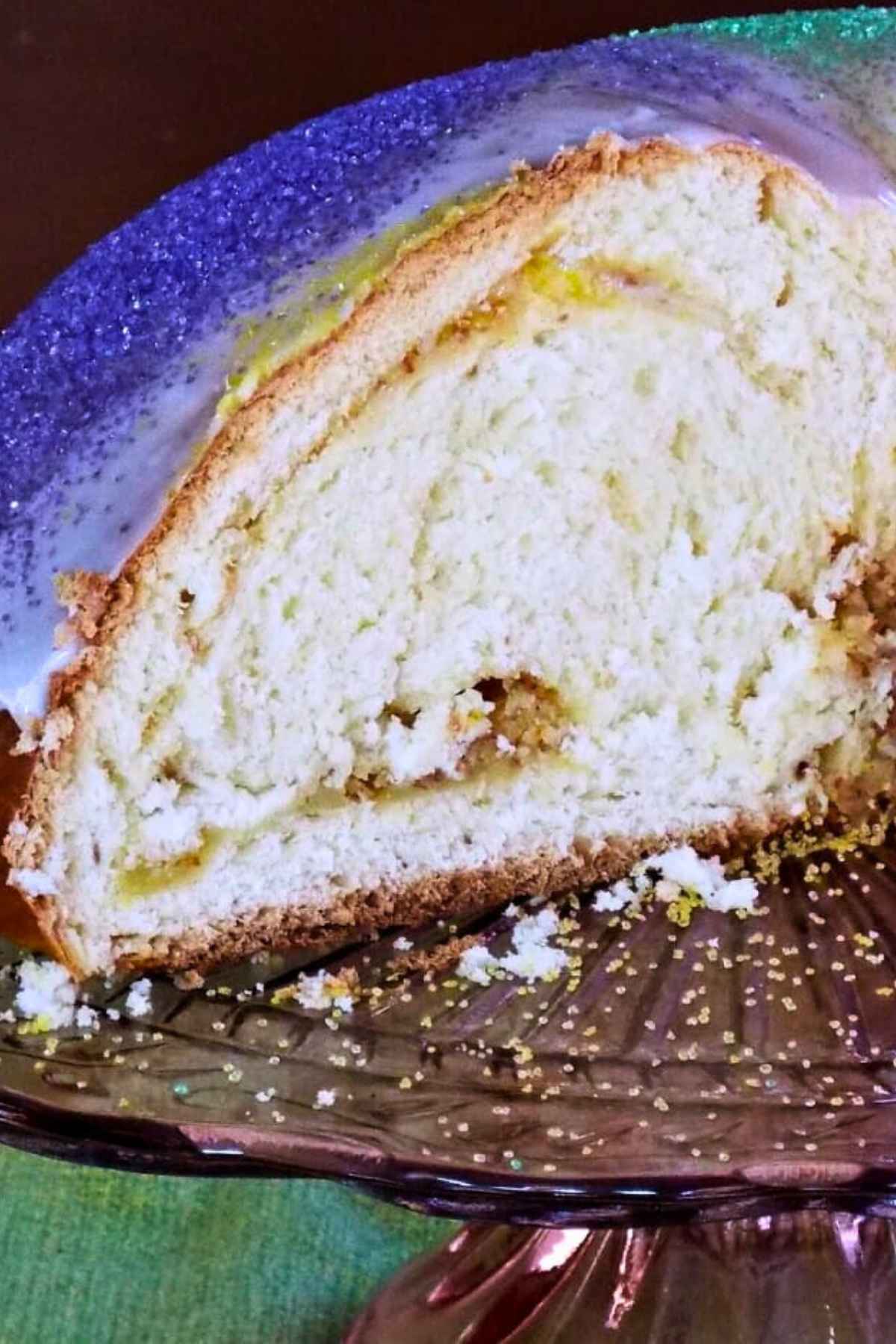 Close-up of a sliced sweet bread with almond filling and colorful sugar sprinkles on a purple glass stand.