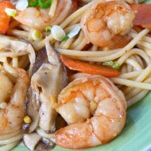 Close up of longevity noodles featuring stir-fried shrimp, sliced mushrooms, carrots, and green onions in a savory sauce.