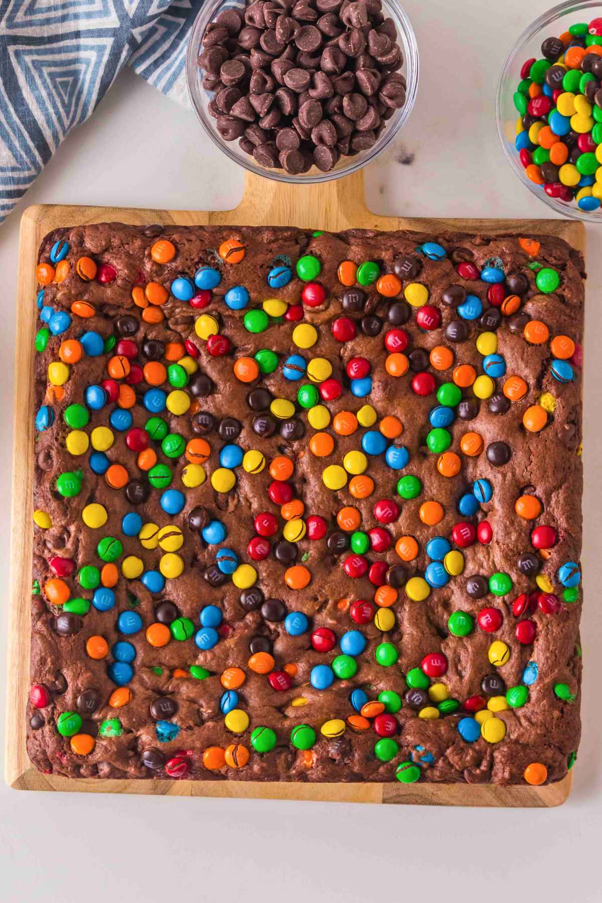 Freshly baked chocolate cake mix brownies topped with a rainbow of M&M candies on a wooden board.