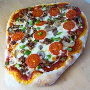 A rustic homemade pizza with a make ahead pizza crust topped with melted mozzarella, tomato slices, green peppers, mushrooms and beef like crumbles.