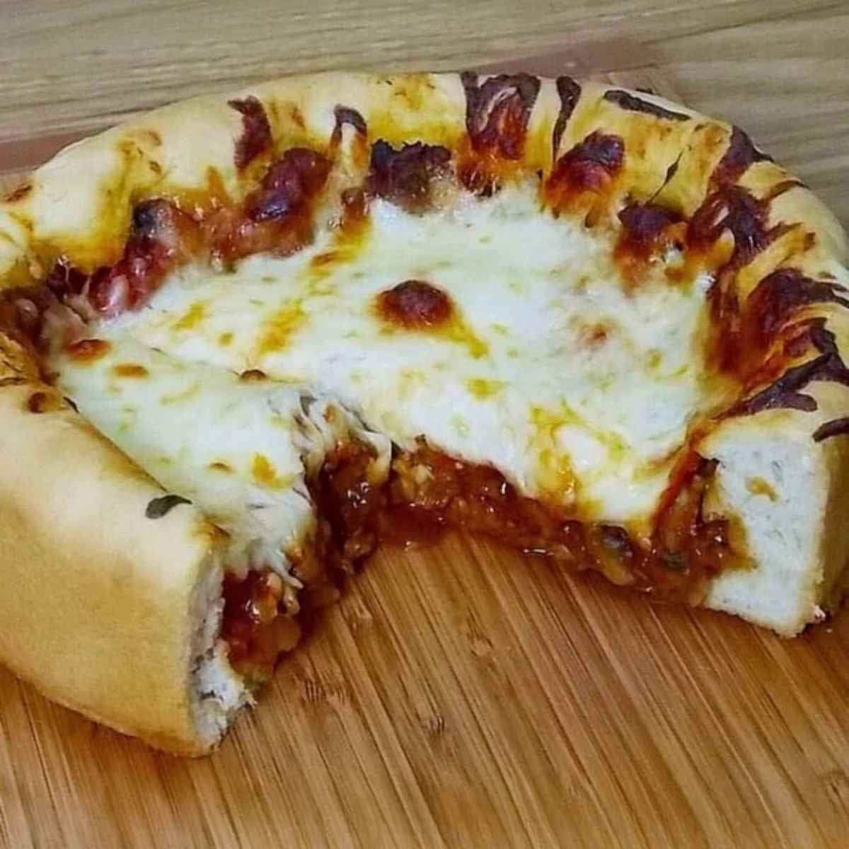 A thick, deep dish Mushroom Sausage Pizza with a golden brown crust, melted mozzarella cheese, and savory toppings, sliced and served on a wooden curring board.