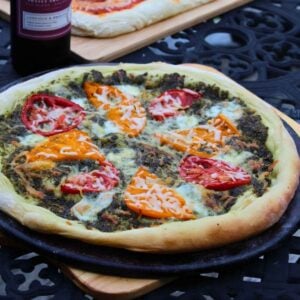 Pesto pizza with fresh tomato slices and mozzarella on a well seasoned pizza stone.