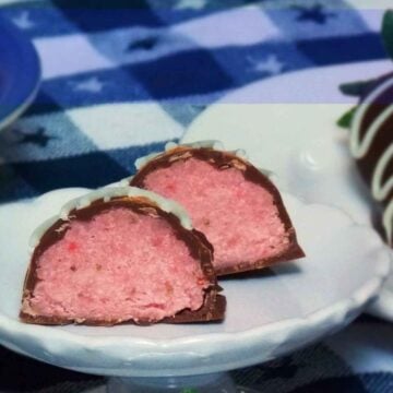 Two strawberry cake balls cut in half, showing a moist pink cake center coated in a white and dark chocolate, served on a white scalloped plate.