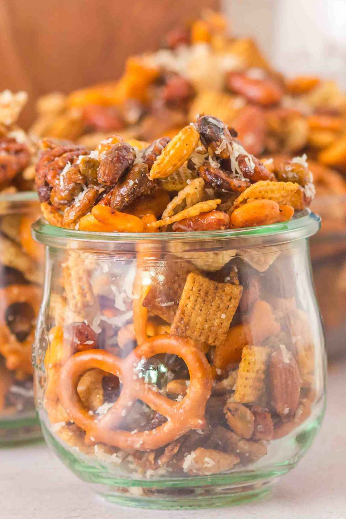 A glass jar with homemade sweet and salty snack mix with a large glass bowl of mix blurred in the background.