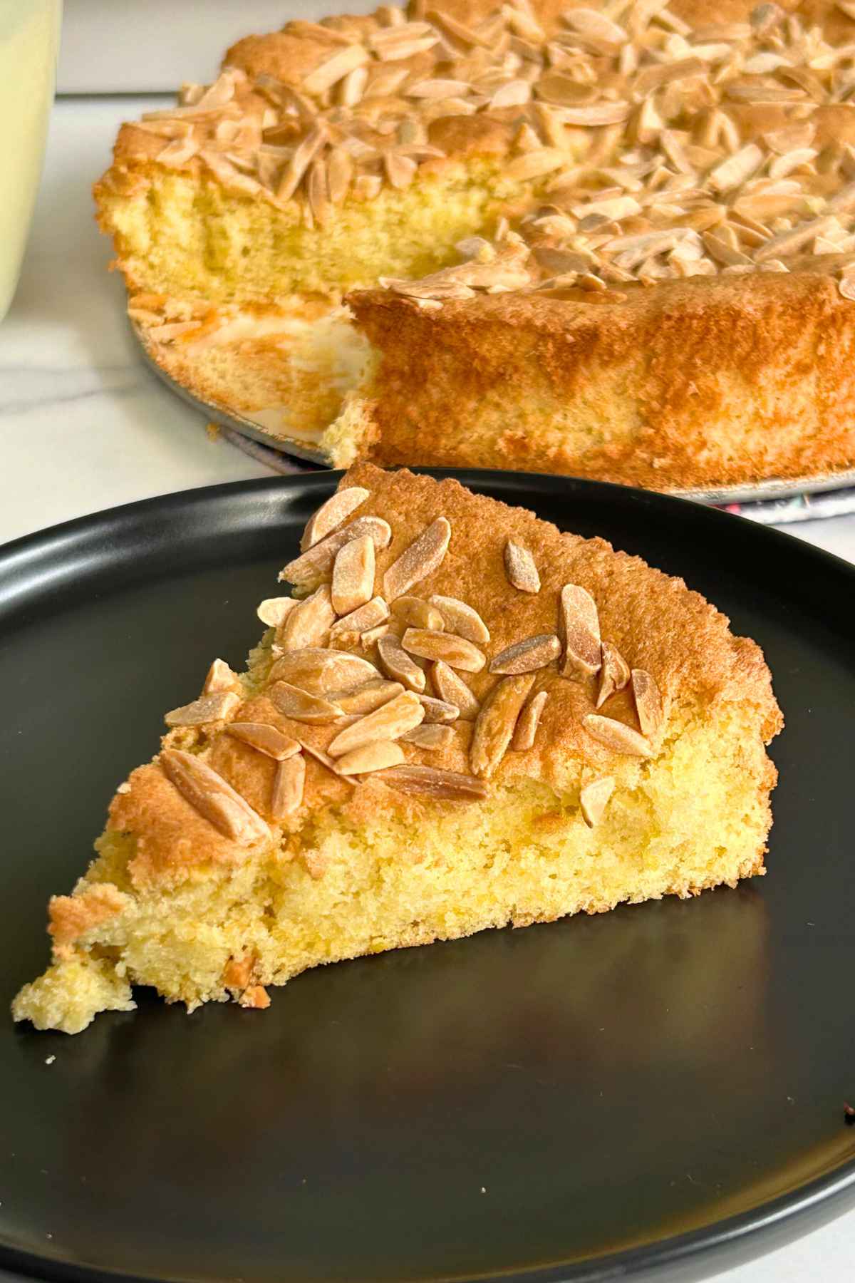 A slice of almond cake on a black plate.
