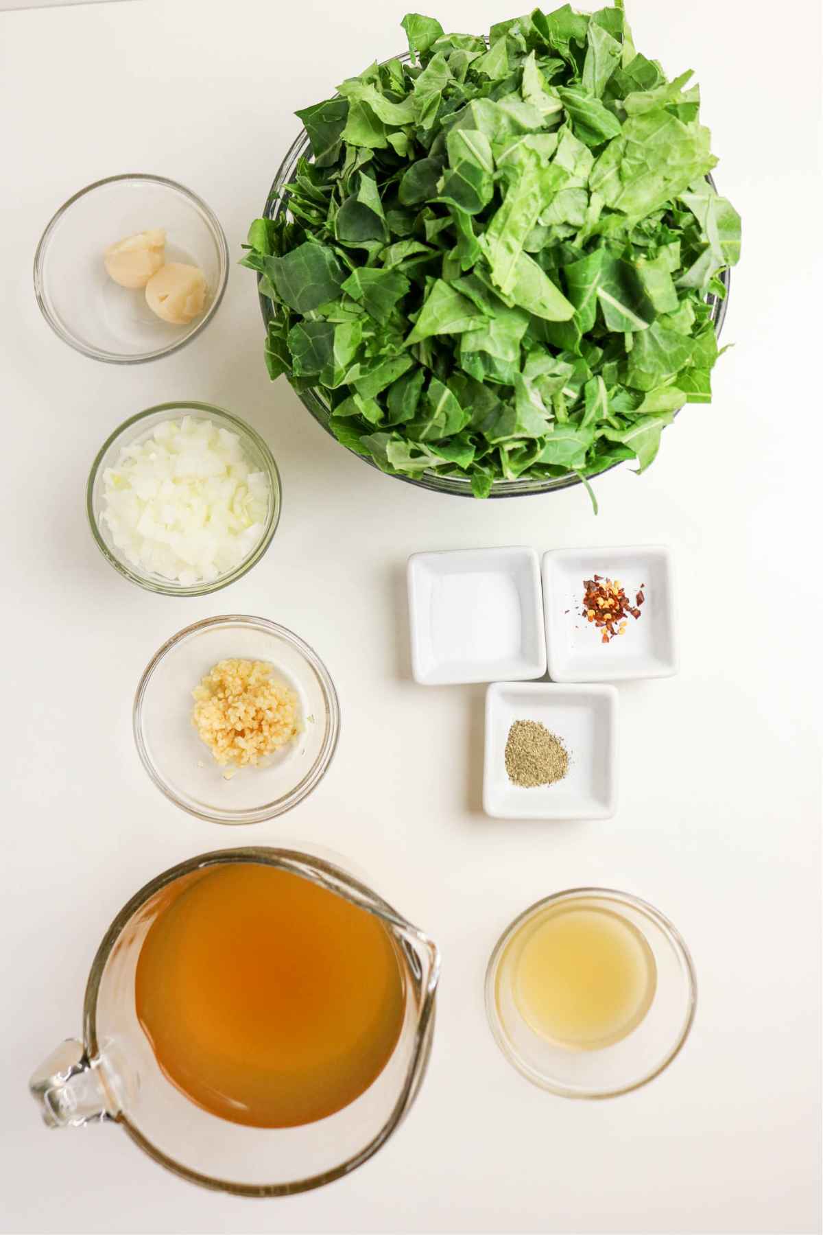 Overhead view of fresh ingredients for Southern greens including chopped leaves, chicken broth, garlic, and onions.