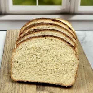 Several thick slices of homemade buttermilk bread stacked on a wooden cutting board, showing a soft, airy crumb and a golden brown crust.
