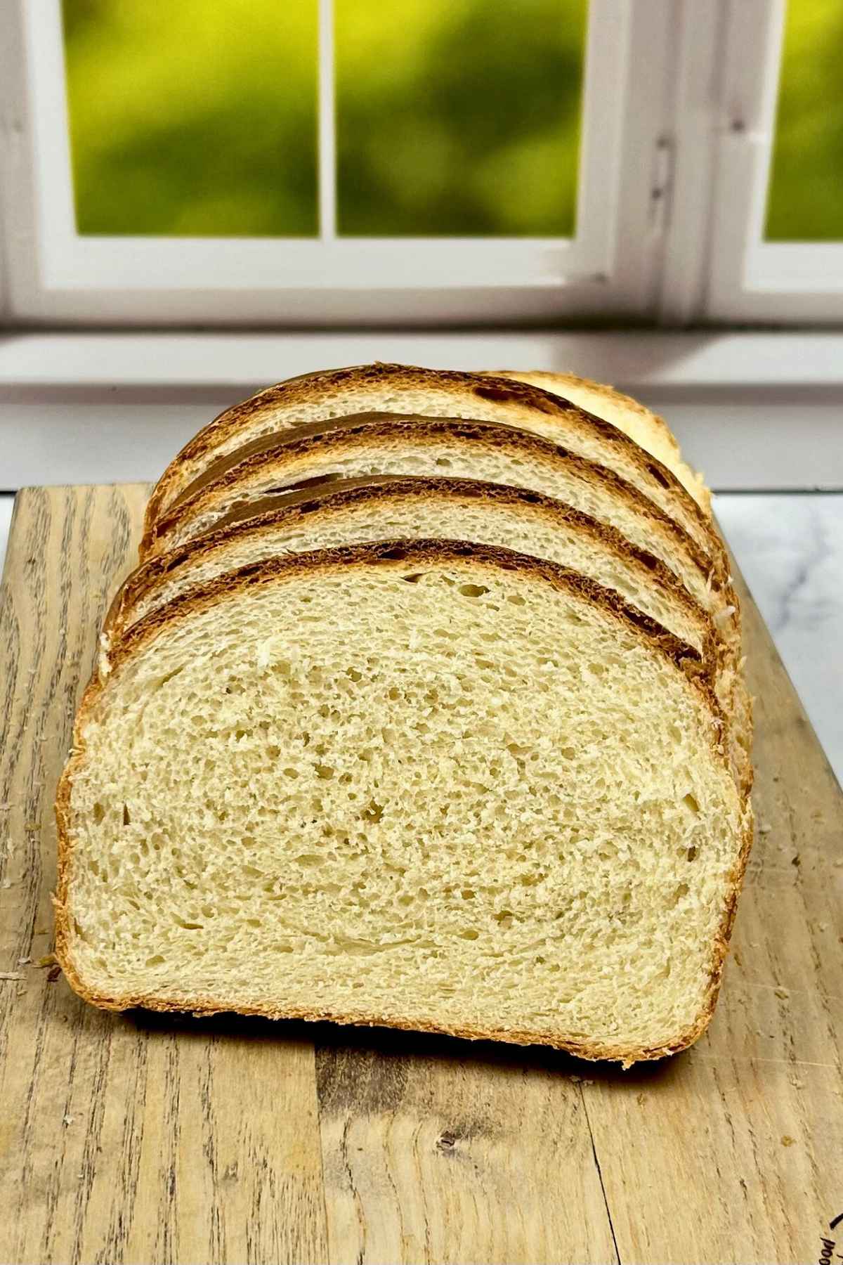 Several thick slices of homemade buttermilk bread stacked on a wooden cutting board, showing a soft, airy crumb and a golden brown crust.