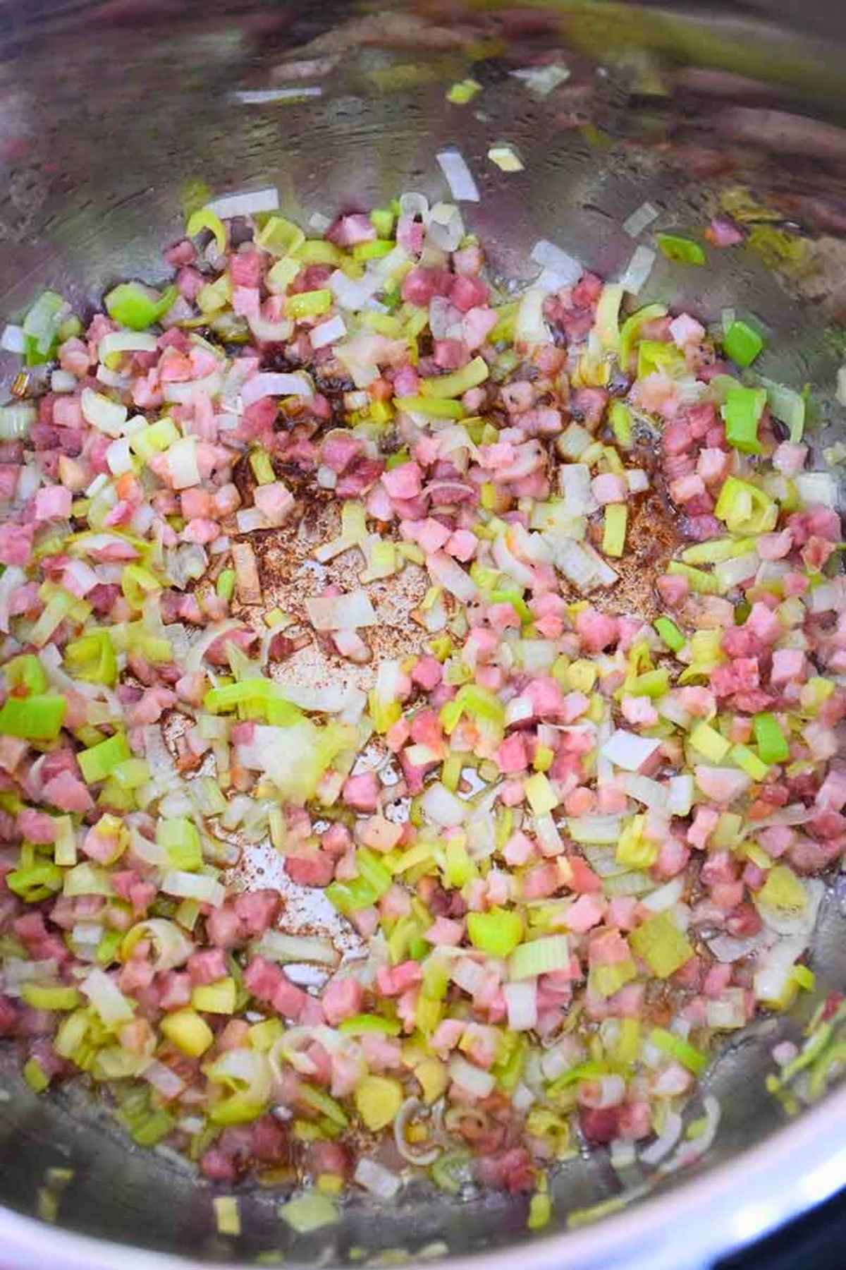 Diced pancetta and chopped leeks being sauteed in a stainless steel pot.