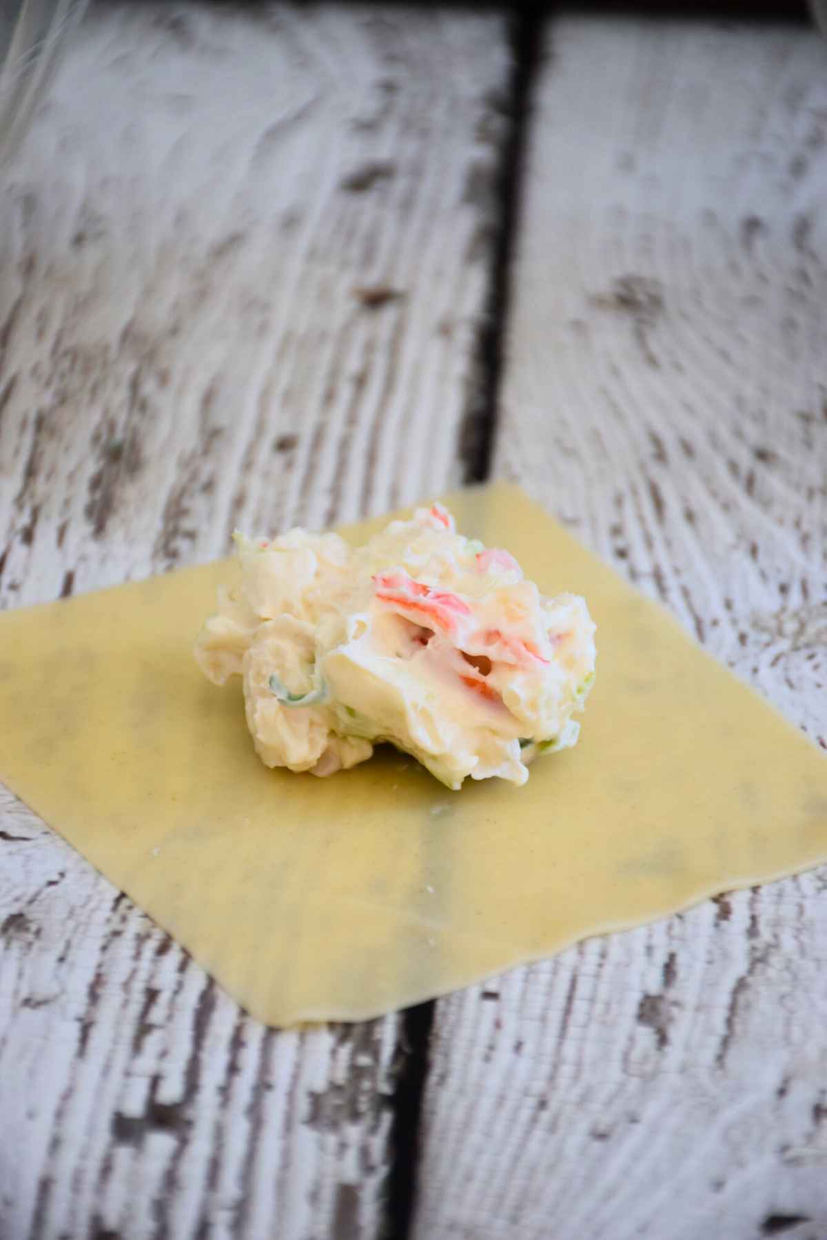 A scoop of creamy seafood and green onion filling centered on a square dough wrapper.