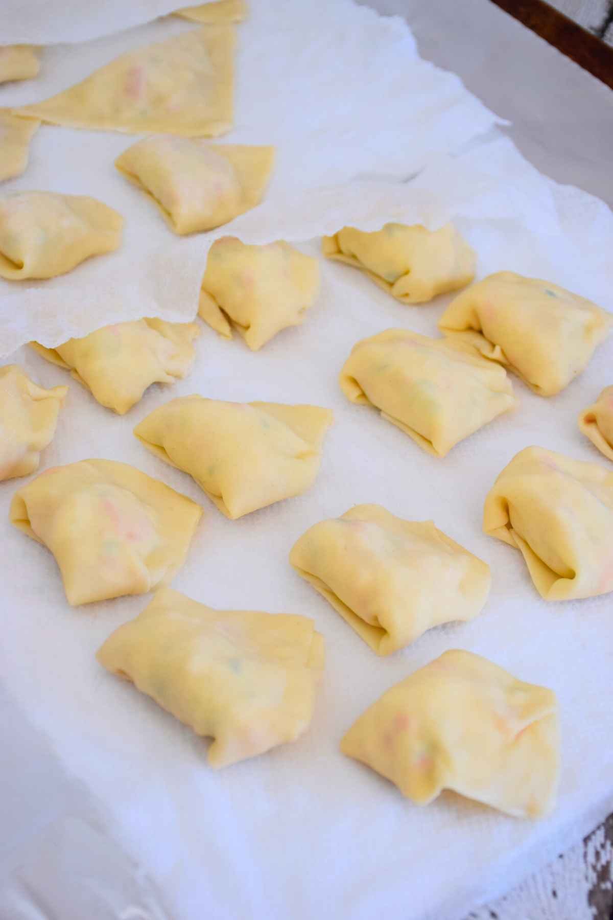 Rows of freshly folded wonton appetizers resting on white parchment paper.