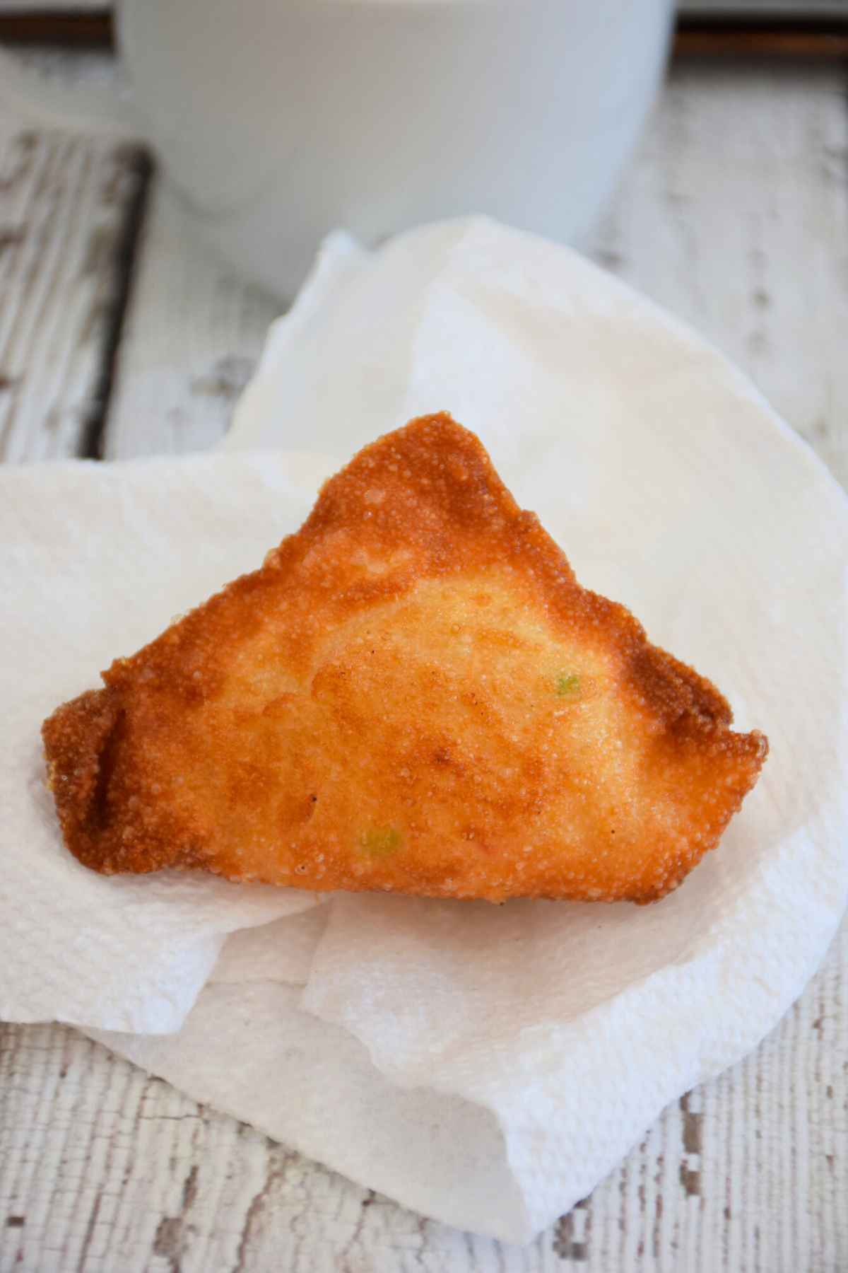 A golden-brown crispy fried Crab Rangoon sitting on a white paper napkin.